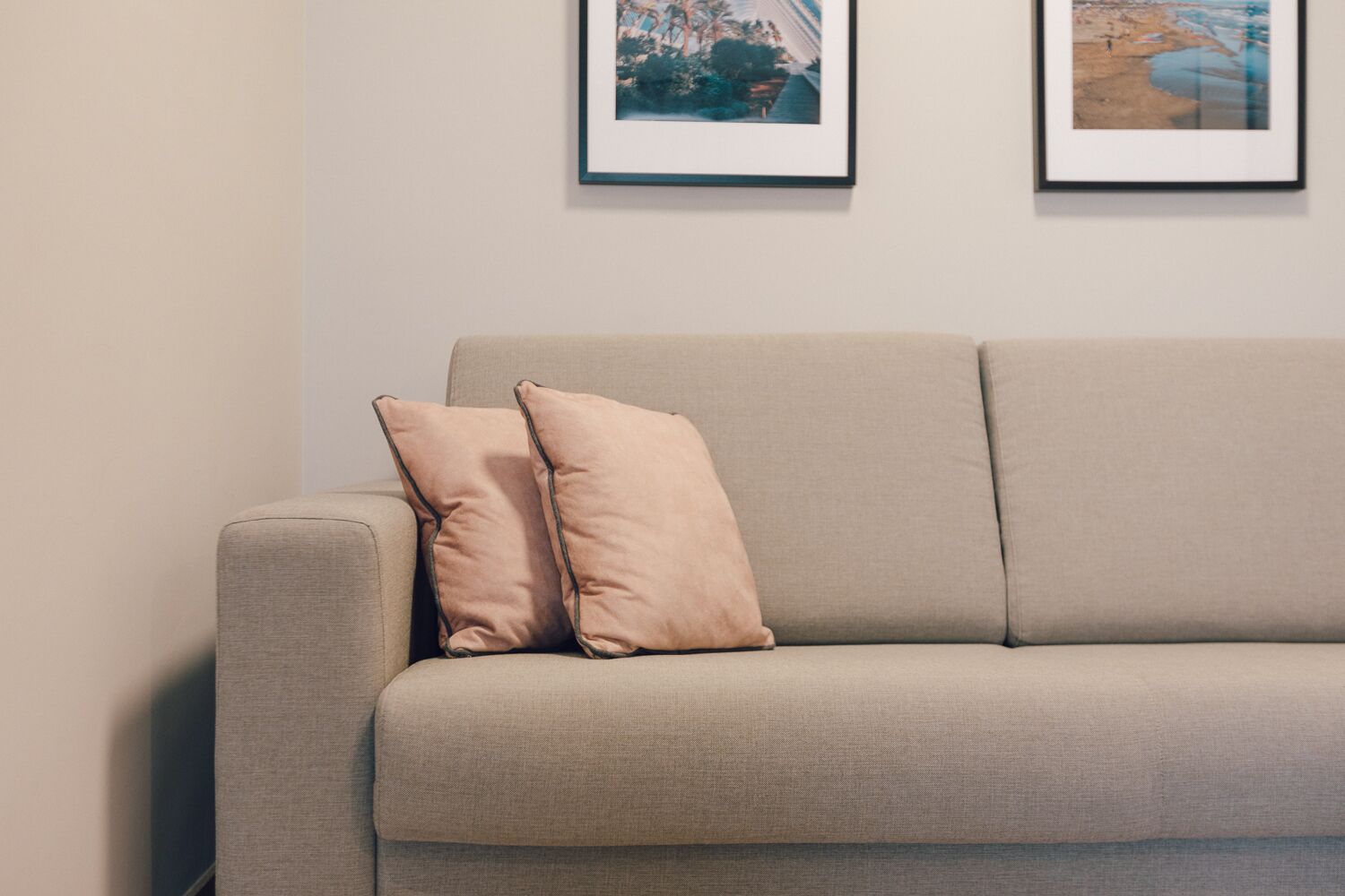 A beige sofa with two matching cushions against a plain wall.