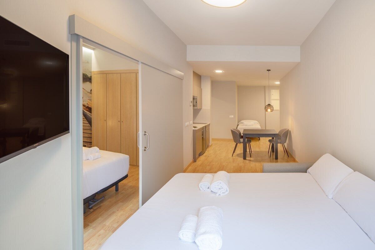 Moderni hotellihuone, jossa on sänky, työpöytä, tuoli, televisio ja kylpyhuone, joka näkyy avoimen oven läpi.
