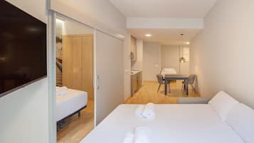 A modern hotel room with a bed, a desk, a chair, a TV, and a bathroom visible through an open door.