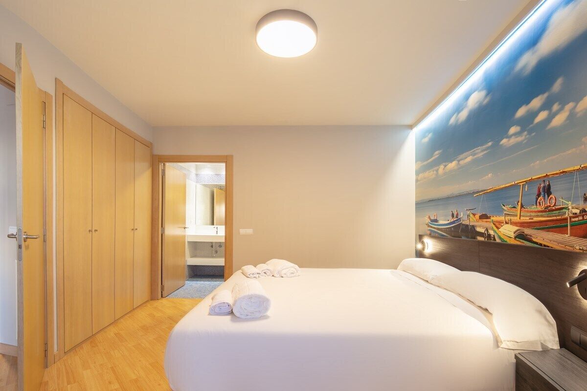 A hotel room with a bed, a painting of boats on the wall, and a wooden wardrobe.