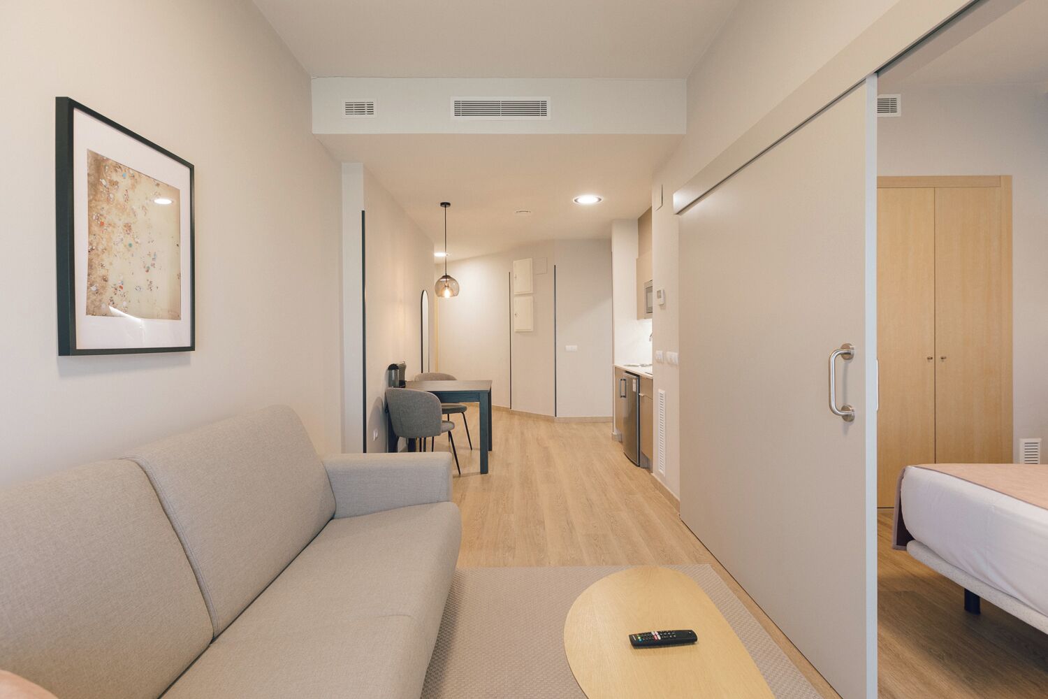 Une chambre d’hôtel moderne équipée d’un canapé, d’une petite table, d’un lit, d’une kitchenette et d’un couloir menant à une autre pièce.