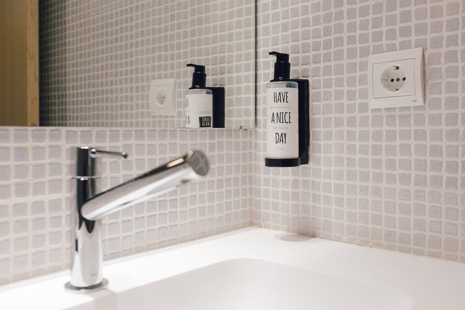A bathroom with a modern sink, a mirror, and two wall-mounted soap dispensers.