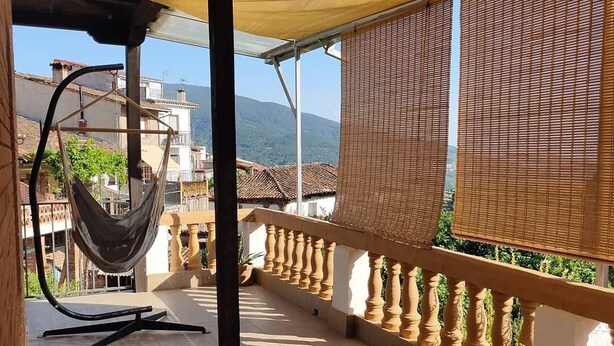 A balcony with a hammock, potted plants, and a view of buildings and mountains. - Casa Rubén Darío, located in the Sierra de Gredos (suitable for pets) (Villarejo del Valle)