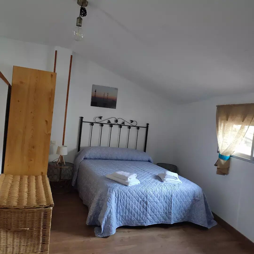 A bedroom with a bed, a nightstand, a lamp, a wooden chair, and a window with curtains.
