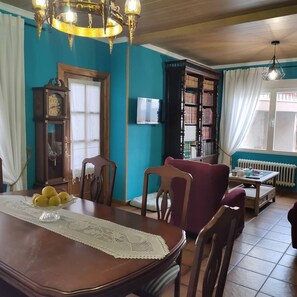 A dining area with a wooden table, chairs, a chandelier, a clock, and a bookshelf.