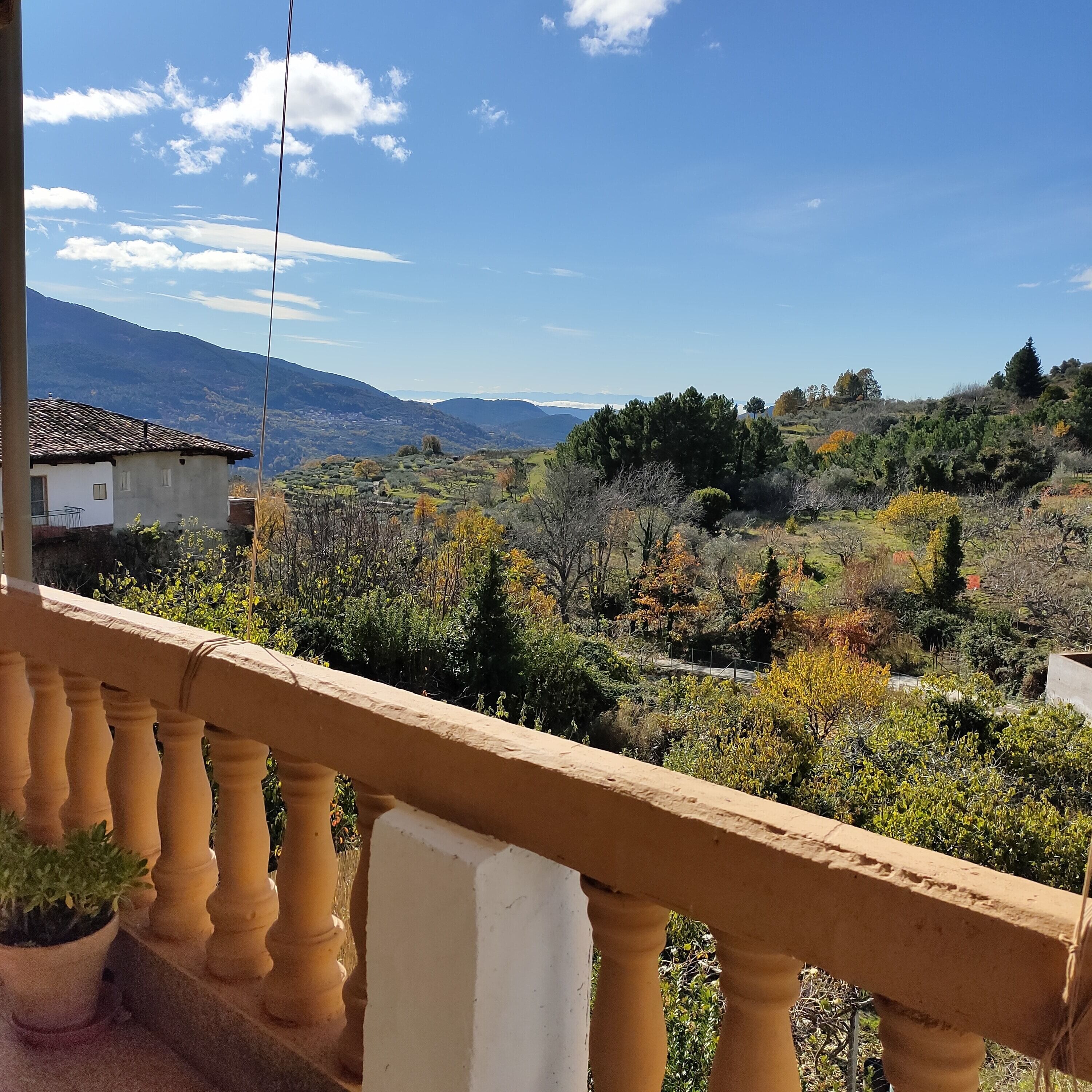 A balcony with a view of a mountainous landscape, a building with a tiled roof, and a railing.