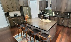 A modern kitchen with dark wood cabinets, a central island with bar stools, a stainless steel refrigerator, a gas stove, and a sink.