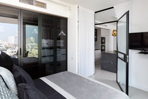A modern bedroom with a large bed, a sliding glass door to a balcony, and a view of the cityscape.