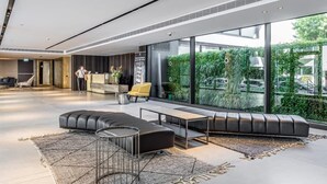 A modern lobby with a reception desk, seating area, and large windows offering a view of greenery and a parking lot. - MAMAD Luxury Executive 4BR with Terrace & Sea View by FeelHome (Tel Aviv - Jaffa)