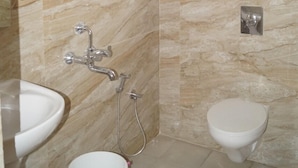 A bathroom with marble walls, a toilet, a sink, and a shower. - BSK Deluxe Lodging (Bengaluru)
