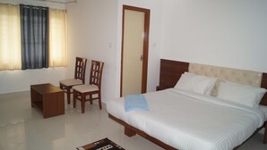 A bedroom with a bed, a chair, a small table, and a door. - BSK Deluxe Lodging (Bengaluru)