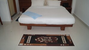 A neatly made bed with a blue towel, a wooden headboard, and a decorative rug on a tiled floor. - BSK Deluxe Lodging (Bengaluru)