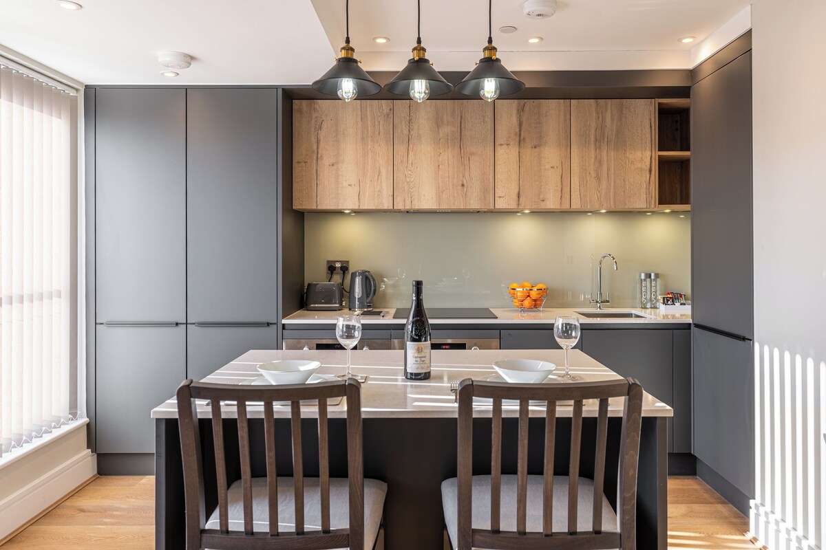 A modern kitchen with grey cabinets, wooden accents, and pendant lighting.