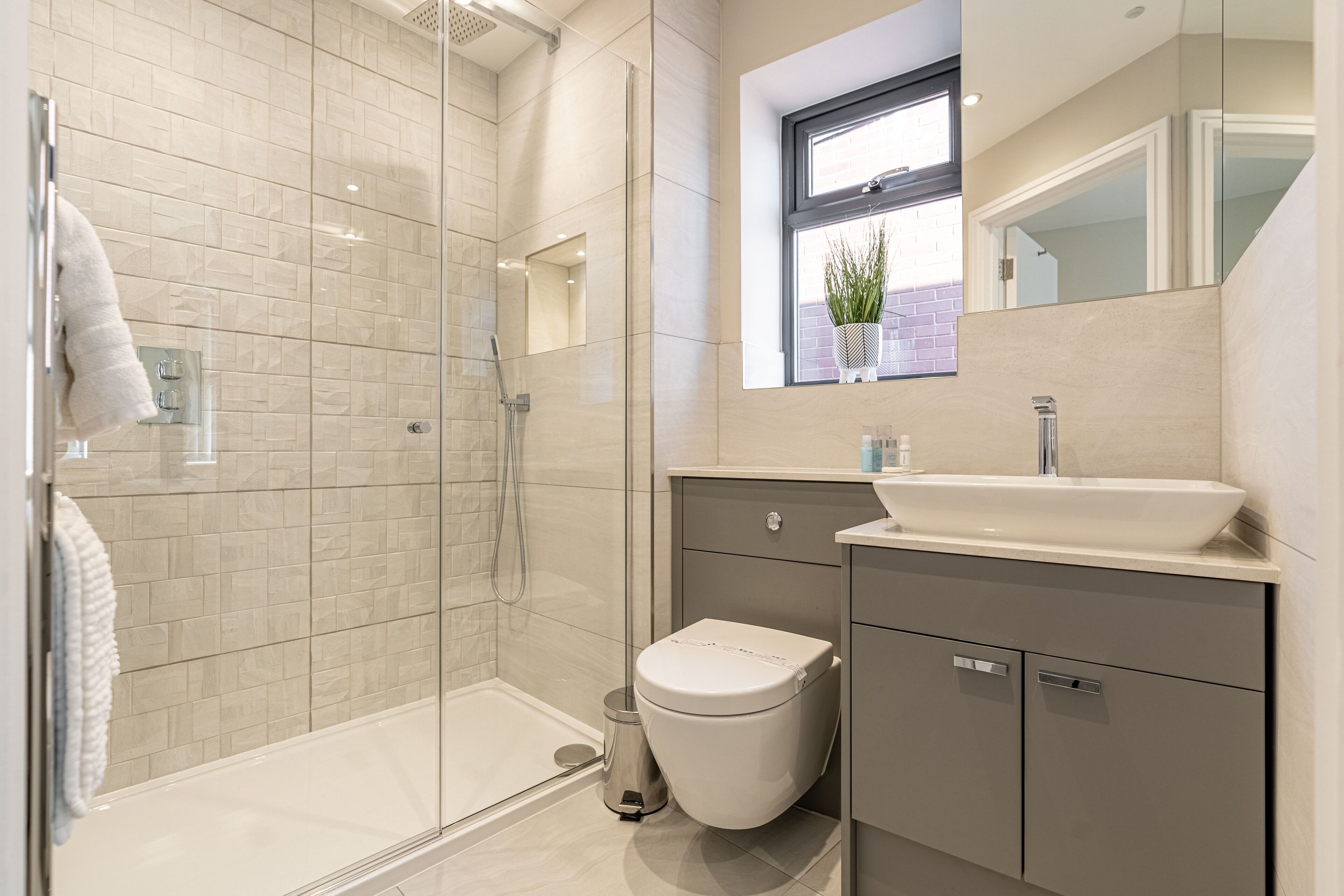 Un baño moderno con ducha de vidrio, inodoro blanco y tocador con lavamanos y espejo.