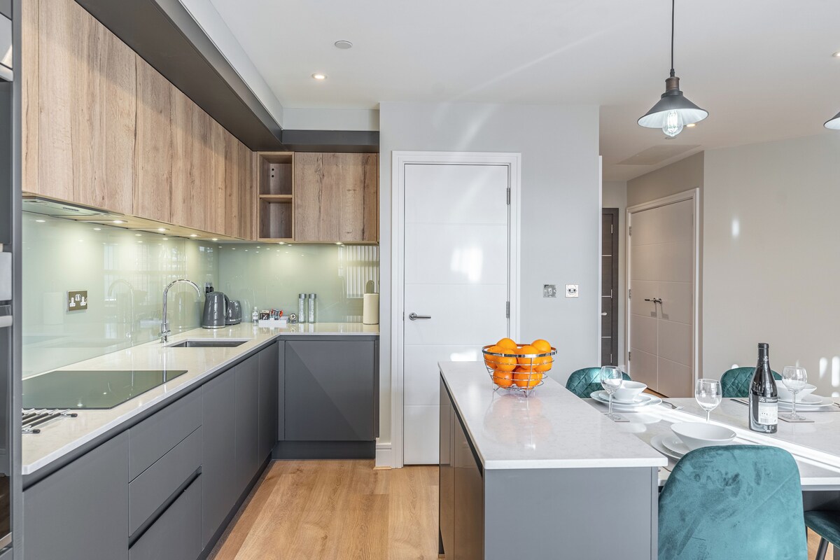 A modern kitchen with grey cabinets, a white countertop, and a wooden floor.