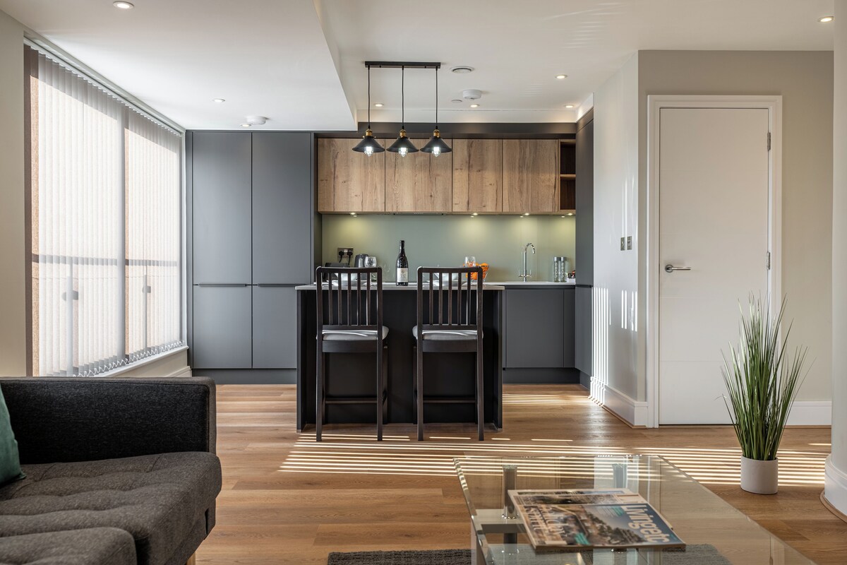 A modern kitchen with dark cabinetry, a central island with bar stools, and pendant lighting.