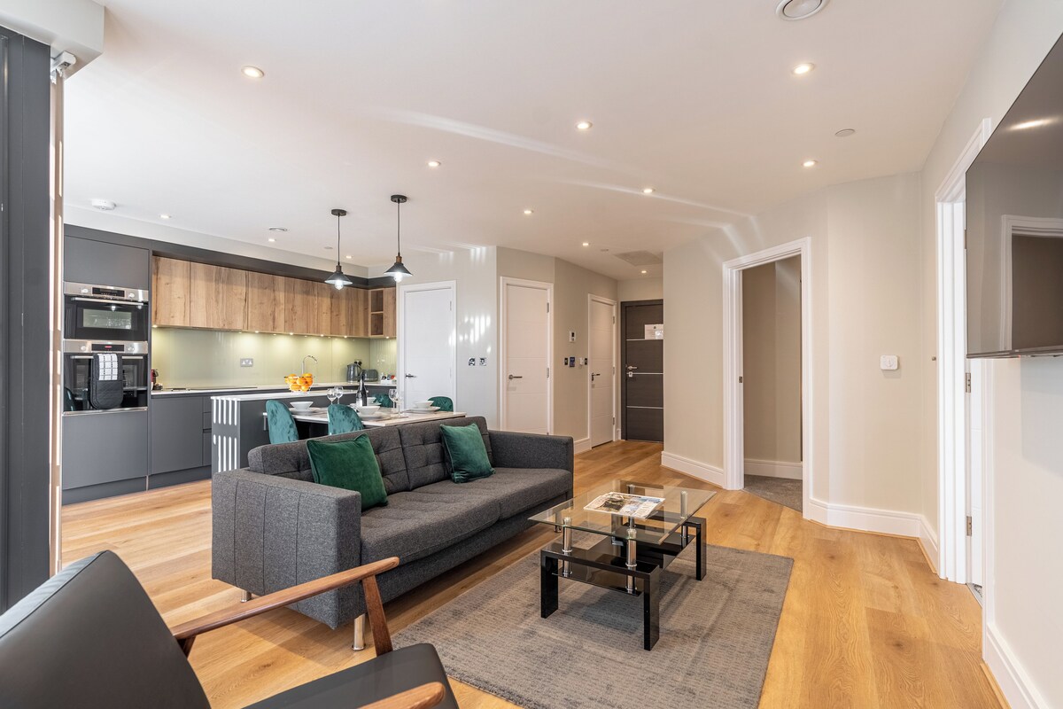 A modern living room with a grey sofa, a glass coffee table, and wooden flooring.