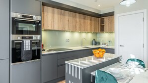 Una cocina moderna con armarios grises, horno empotrado, lavabo y comedor con mesa y sillas blancas.