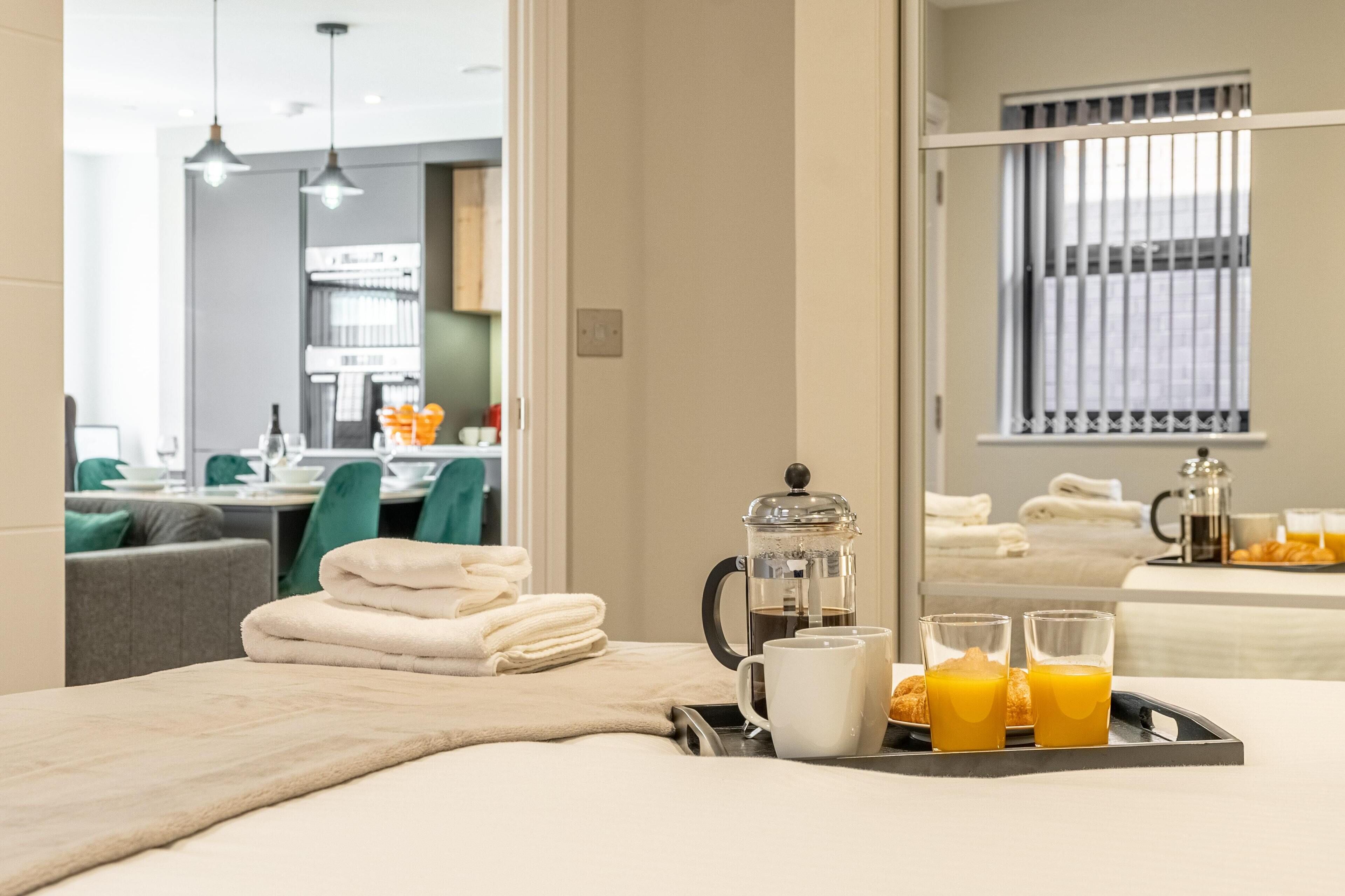 A hotel room with a bed, a tray with breakfast items, and a view of the kitchen and dining area.