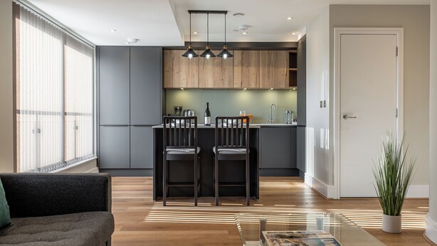 Una cocina moderna con armarios oscuros, una isla central con taburetes de bar e iluminación colgante.