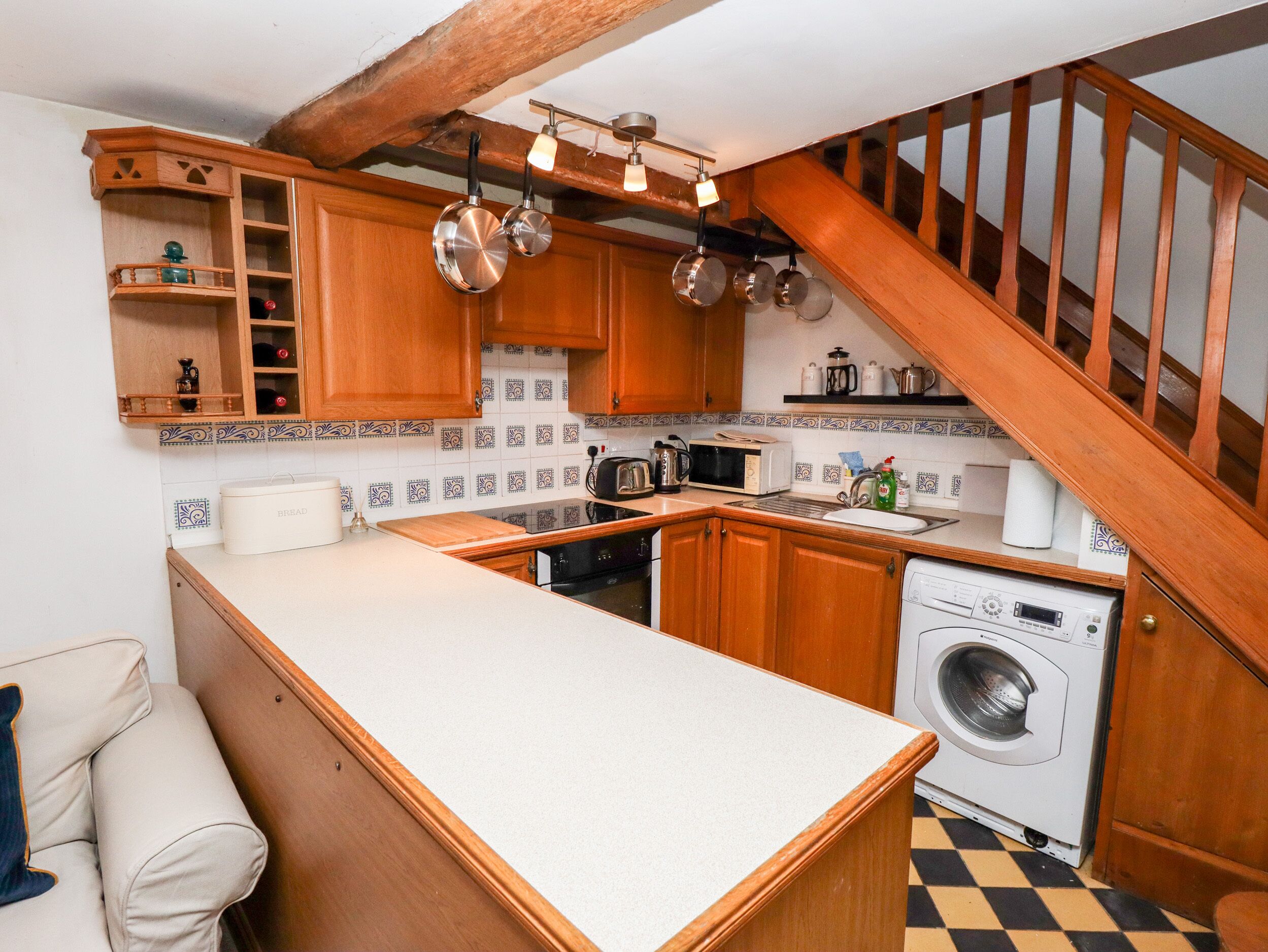 A compact kitchen with wooden cabinets, a microwave, a washing machine, and a coffee maker.