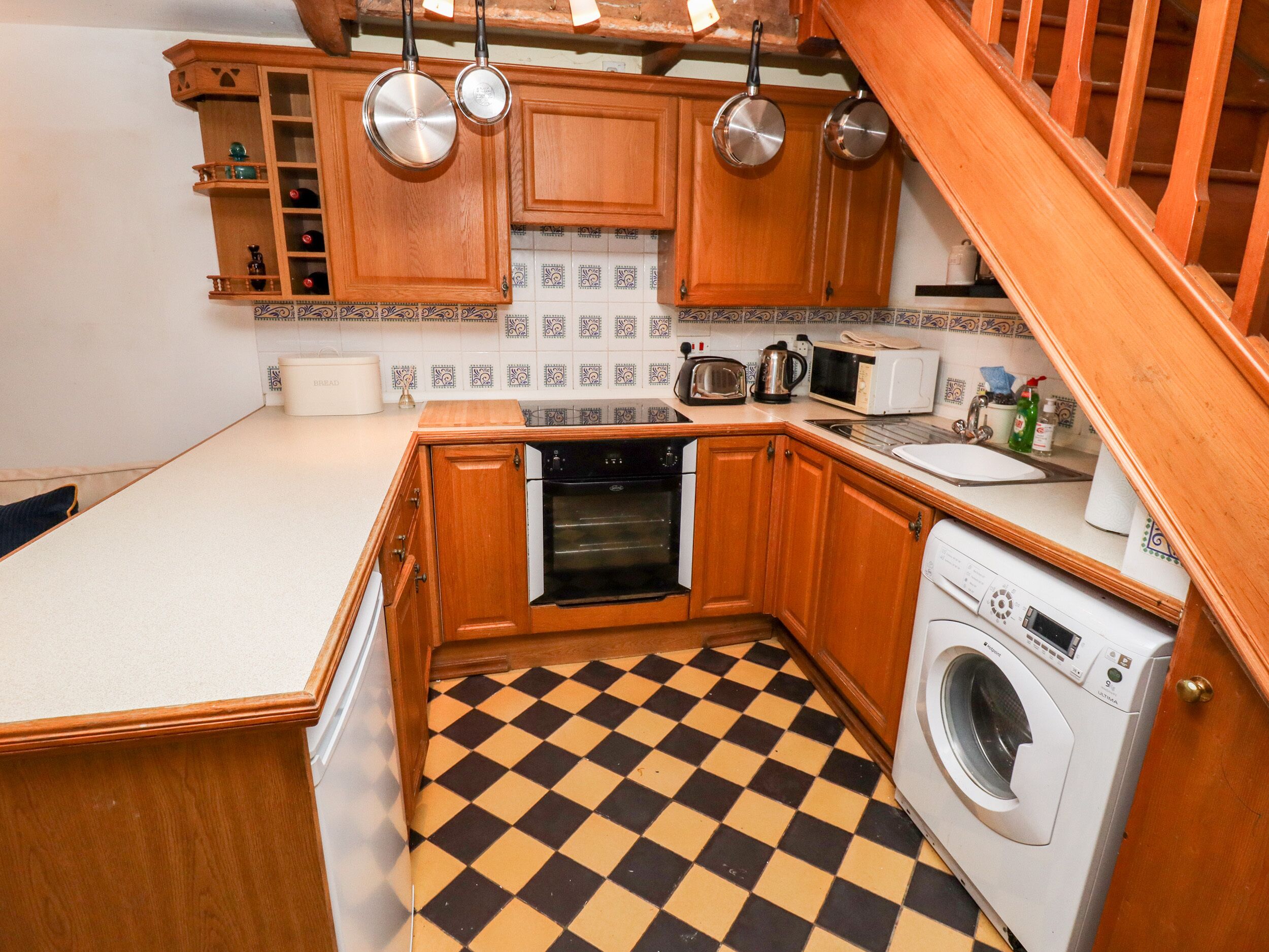 A compact kitchen with wooden cabinets, a built-in oven, a microwave, and a washing machine.