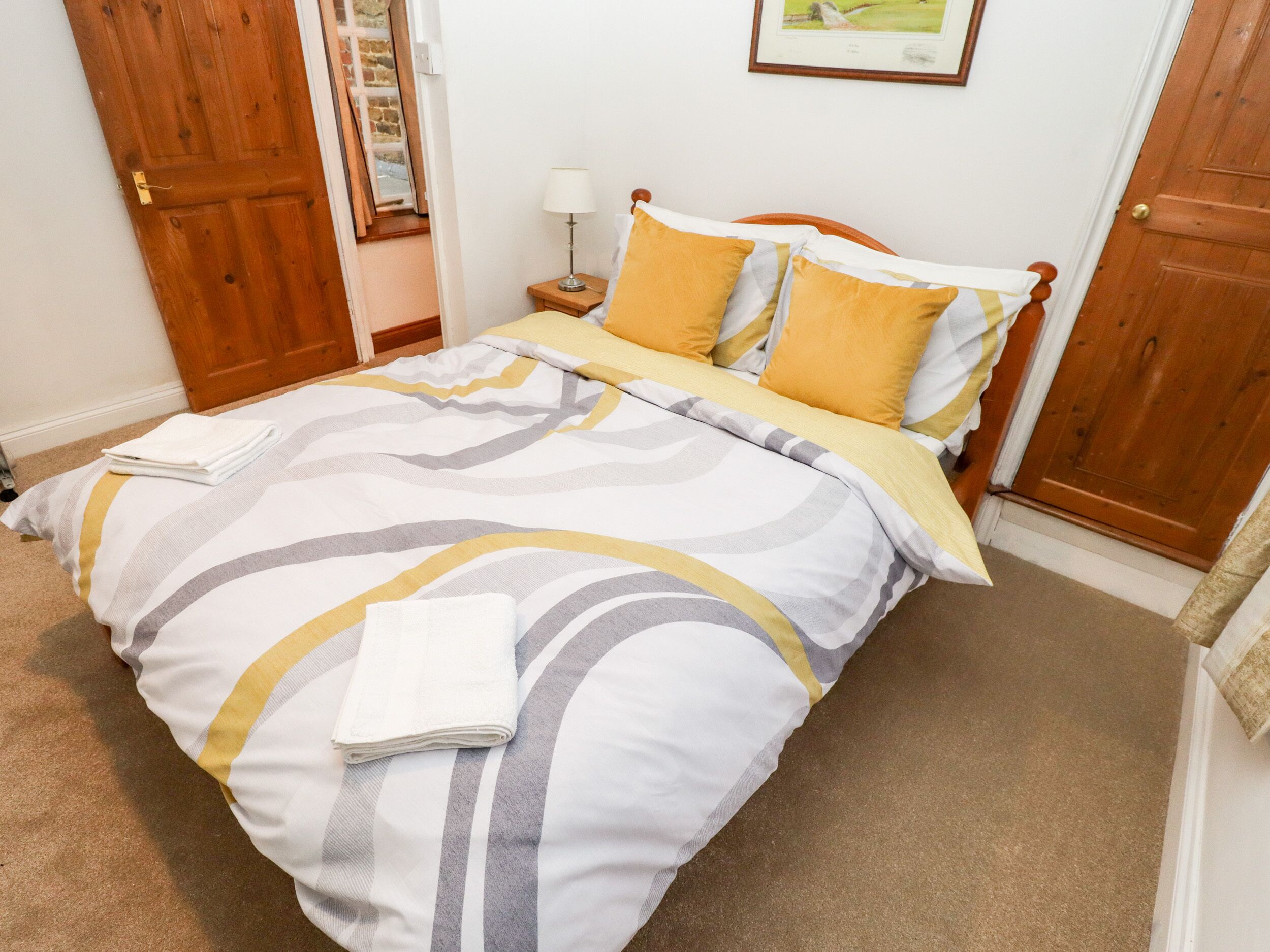 A neatly made bed with striped bedding, a bedside lamp, and a framed picture on the wall.