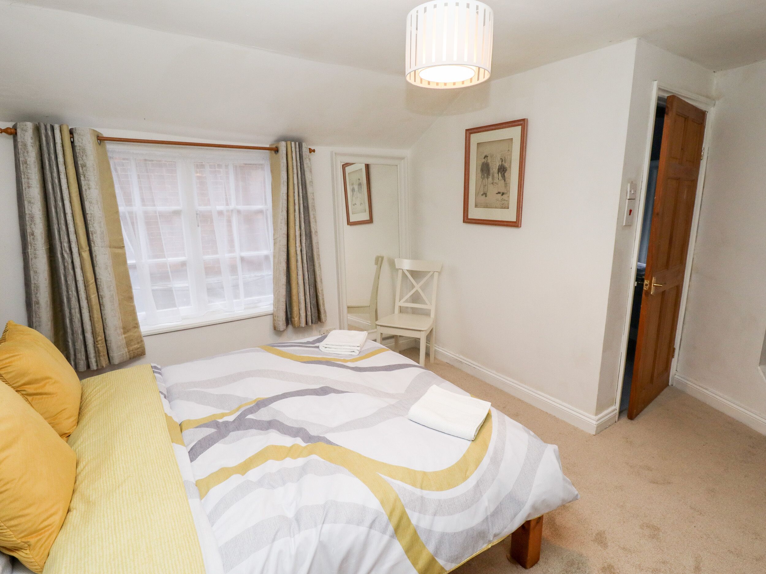 A bedroom with a bed, a chair, a window with curtains, a door, and a light fixture.