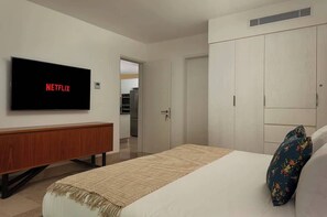 Habitación de hotel con cama, televisor mostrando 'NETFLIX', armario y puerta que da a una kitchenette.