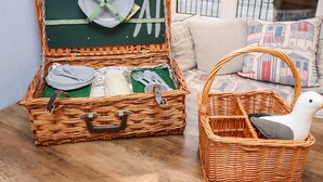 Une valise en osier, avec un intérieur vert, contenant des assiettes, des couverts et une figurine d’oiseau blanche.