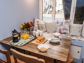 Une table en bois dressée pour le petit-déjeuner, avec une cafetière, des verres de jus d’orange, des croissants et un bol de céréales.