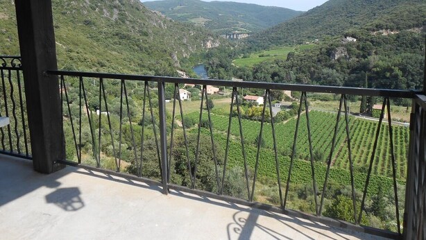 A balcony with a view of a valley, vineyards, and distant buildings.