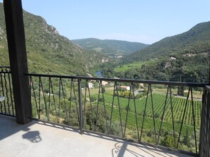 A balcony with a view of a valley, vineyards, and distant buildings.