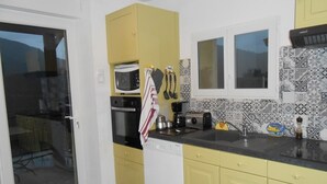 A kitchen with yellow cabinets, a black countertop, a microwave, a toaster, and a window with a view.