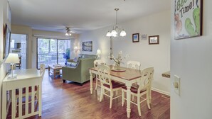 A dining area with a wooden table and chairs, a green sofa, and a ceiling fan. - 2 BR Treetops First Floor easy to access Bikes & Beach Gear included (Hilton Head Island)
