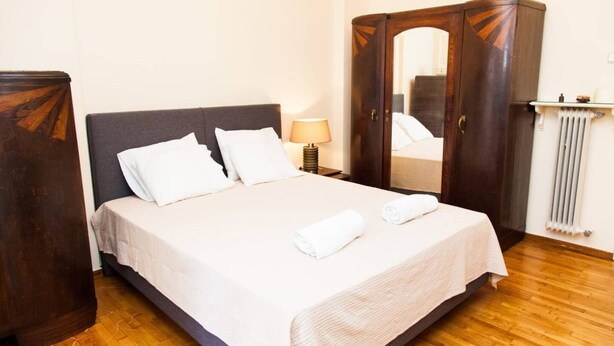 A neatly made bed with white linens, a wooden wardrobe, and a bedside lamp. - Renovated apt in the Heart of Piraeus (Piraeus)