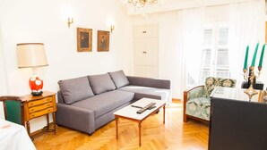A living room with a grey sofa, a small table, a patterned armchair, a lamp, and a chandelier. - Renovated apt in the Heart of Piraeus (Piraeus)