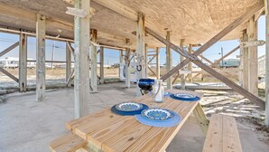 Een terras van hout buiten, met picknicktafels en een barbecue.