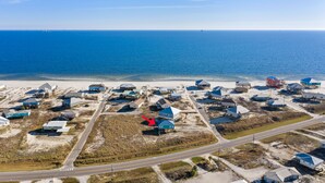 Luchtbeeld van een kustgebied met woningen, een weg en de oceaan op de achtergrond.