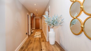 Un corridoio con pavimento in legno, un vaso bianco con piante artificiali e specchi con cornice dorata al muro.