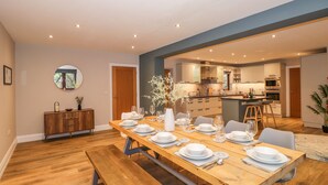 Un'area pranzo moderna con un tavolo in legno apparecchiato per sei persone, una panca in legno e vista sulla cucina.