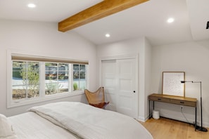 Ein Schlafzimmer mit Bett, Schreibtisch, Stuhl, Fenster mit Blick und einer Tür.