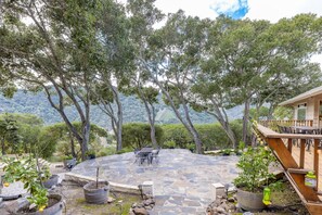 A stone patio with outdoor furniture, surrounded by trees and a mountainous backdrop.