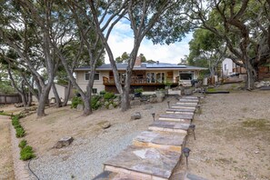 Ein Haus mit einem Kiesweg, der zu einer Terrasse führt, umgeben von Bäumen und einer Kiesfläche.