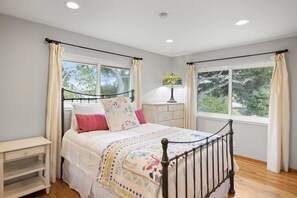 A bedroom with a bed, bedside table, dresser, and a window with curtains.