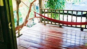 Una terraza de madera con una hamaca de cuerda roja, barandilla y vistas a la vegetación.