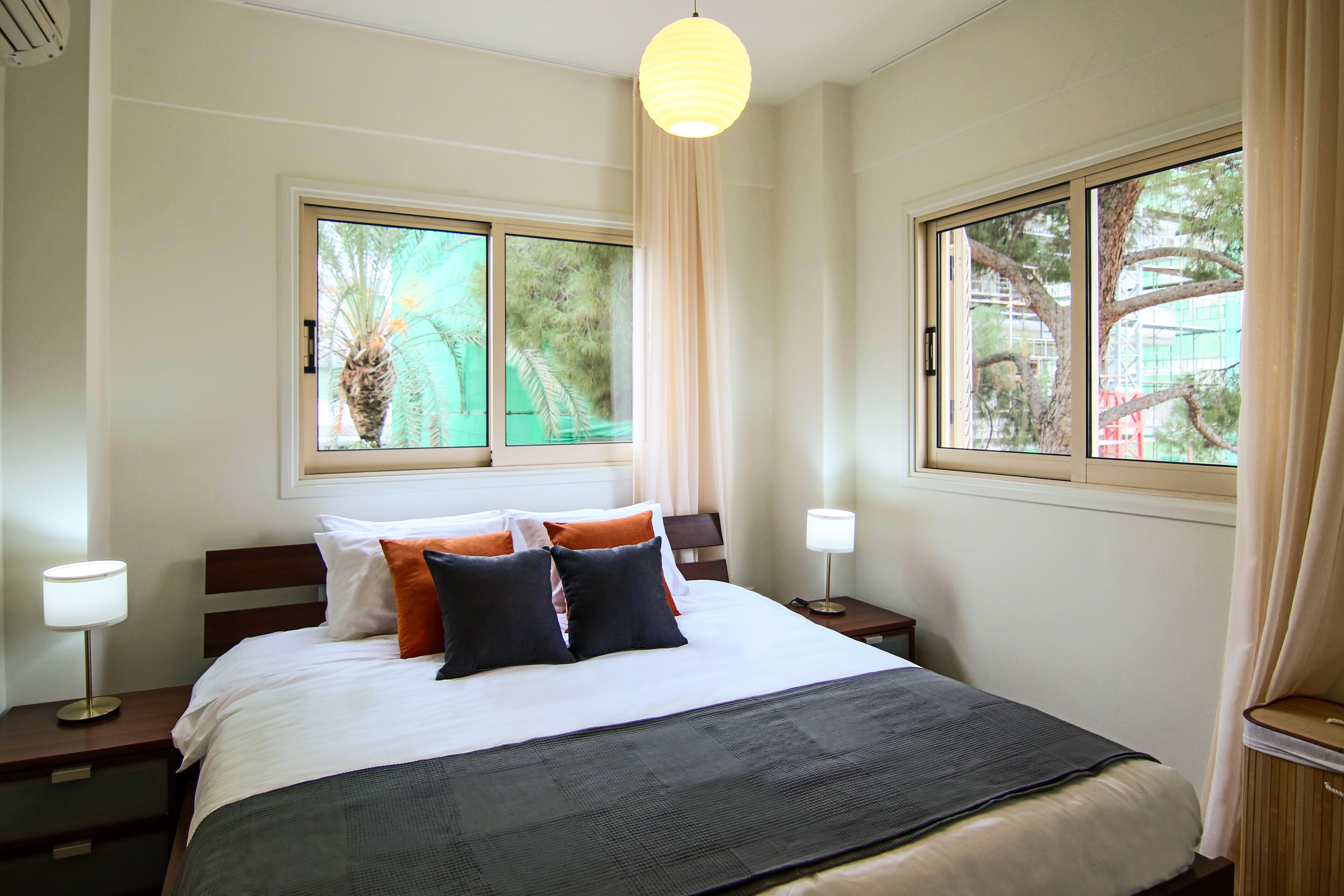 A hotel room with a large bed, two bedside tables, a window with a view of trees, and a hanging light fixture.