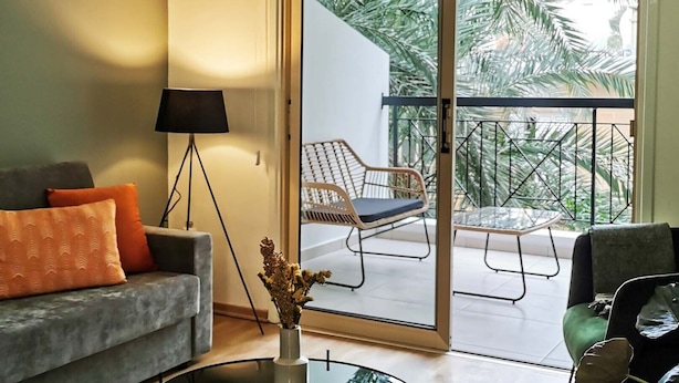 Ein Wohnzimmer mit grauem Sofa, orangefarbenen Kissen, einer Stehlampe und einem Glastisch.
