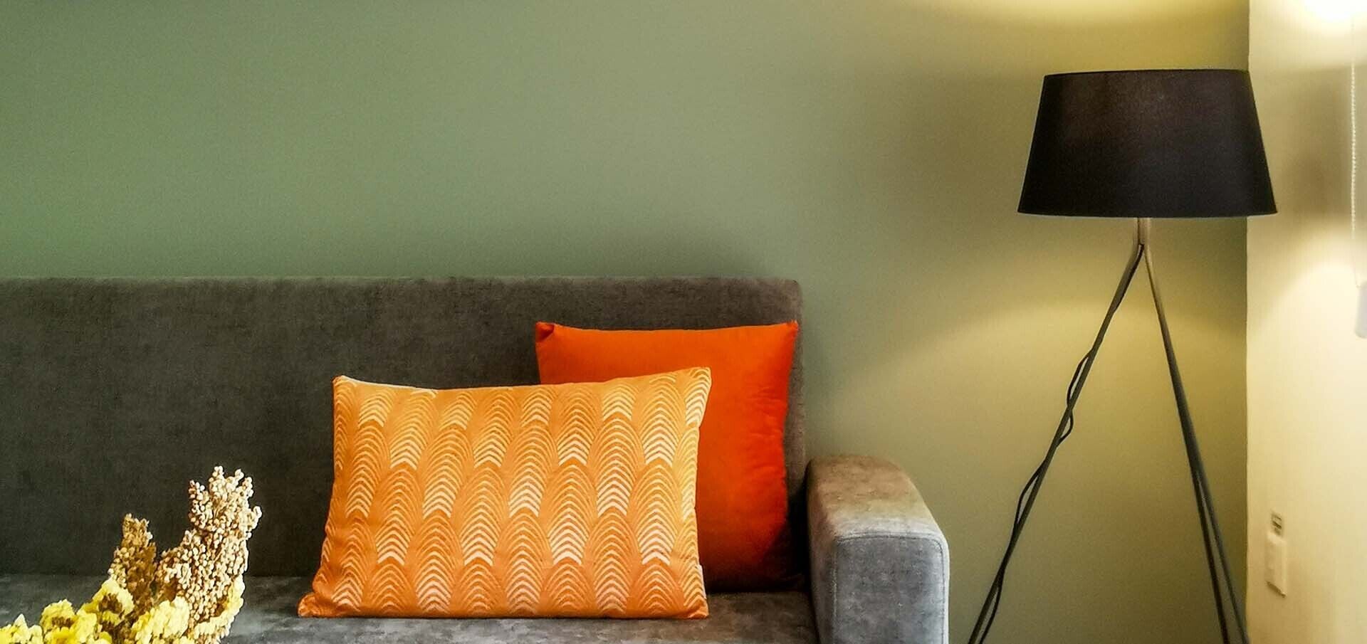 A sofa with two pillows, a floor lamp, and a vase with dried flowers.