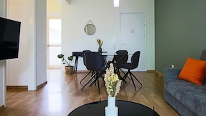 Ein modernes Wohnzimmer mit einem grauen Sofa, einem schwarzen Couchtisch mit Blumenvase und einem Essbereich mit Tisch und Stühlen.